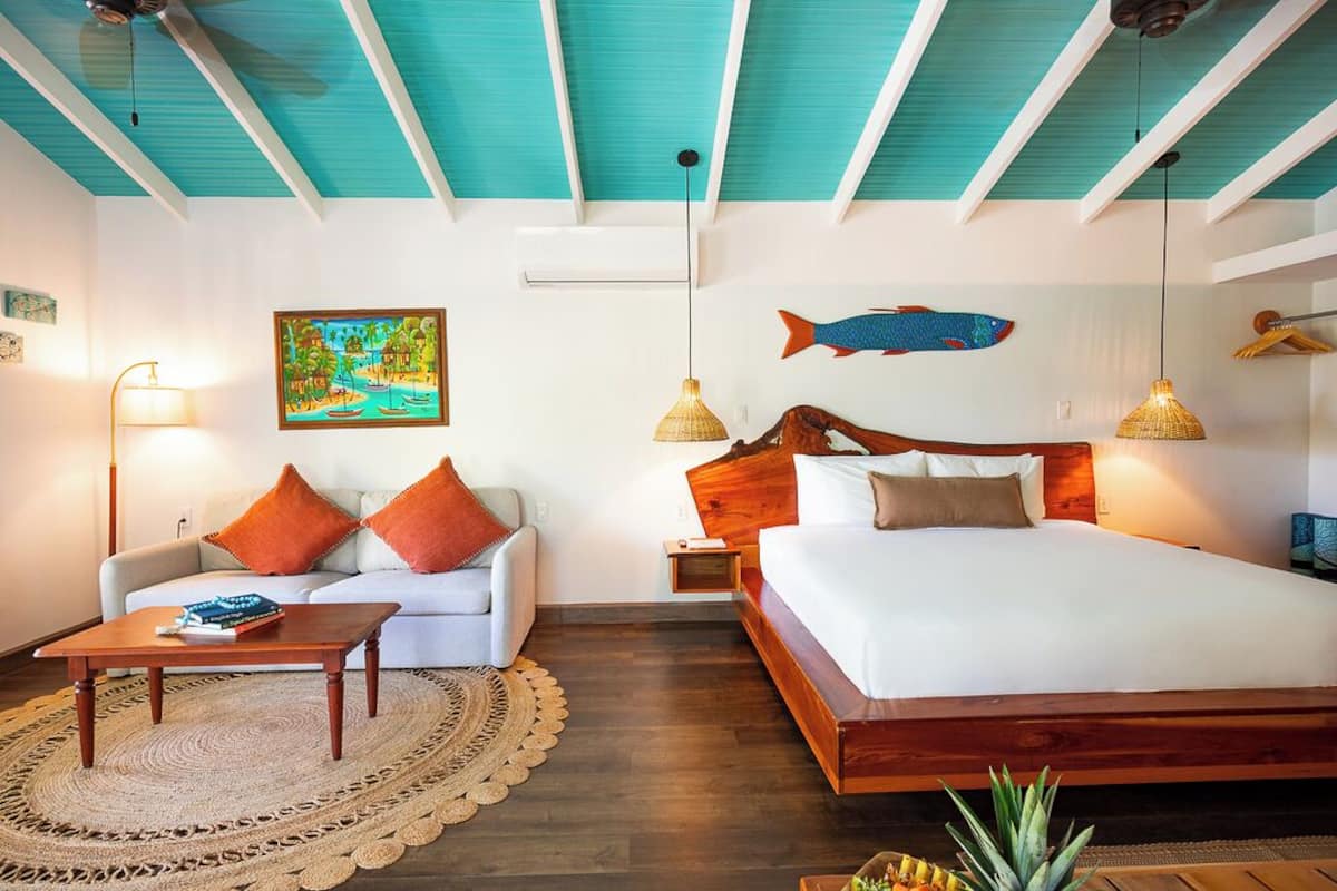 A hotel room with a bed, a sofa, a coffee table, a wall painting, and a fish decoration.