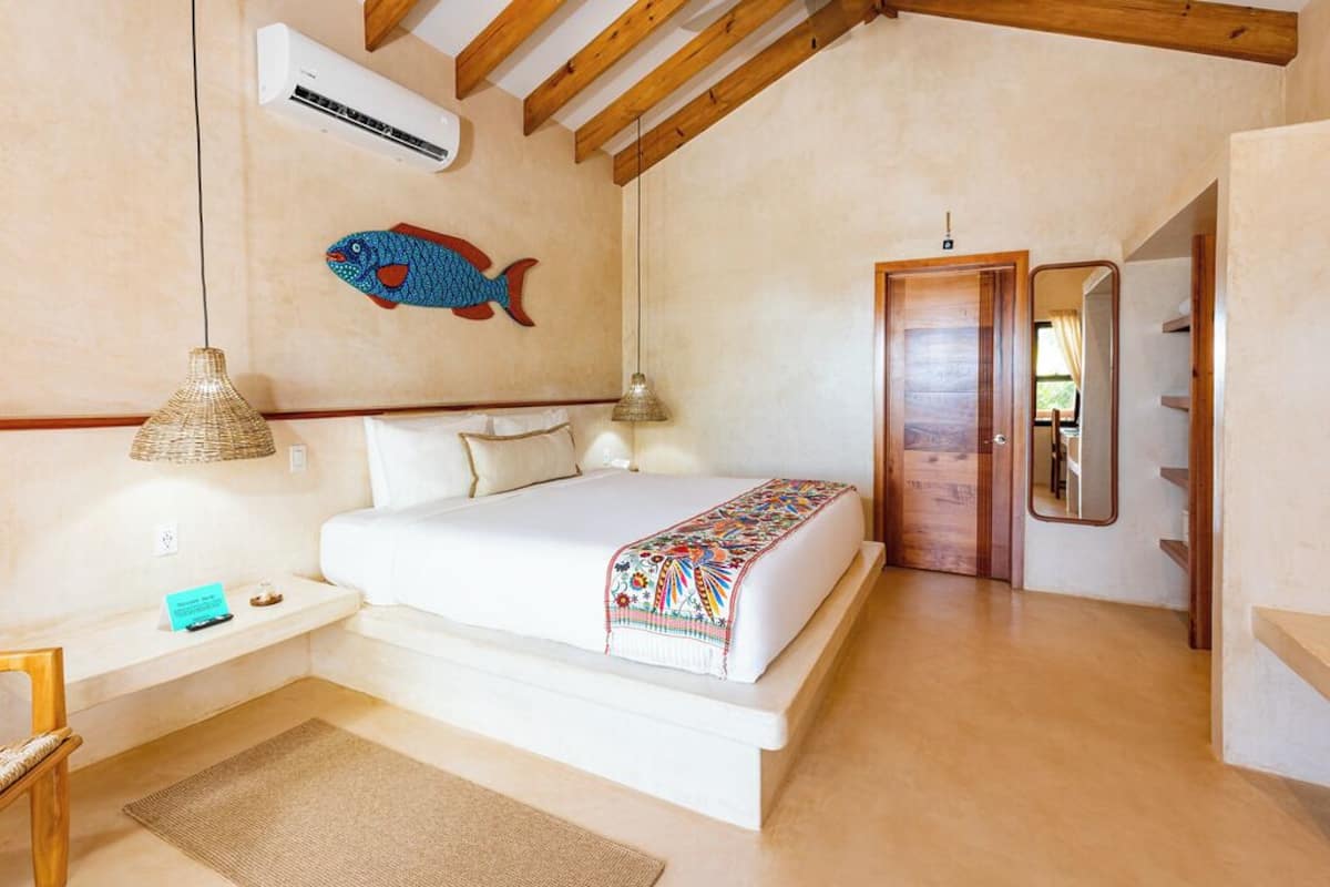 A bedroom with a bed, a bedside table, a lamp, a wall-mounted air conditioner, a fish mural, and a wooden door.