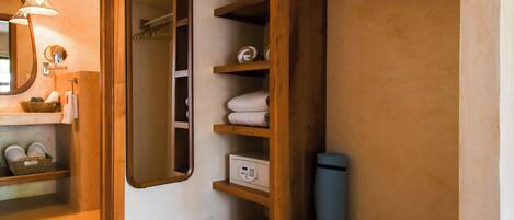 A compact bathroom with a wooden vanity, a mirror, a towel rack, and a small shelf with toiletries.