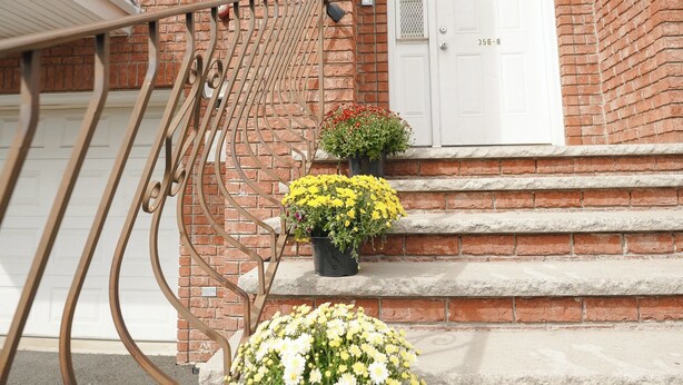 A brick building with a white door, a metal staircase, and potted plants on the steps.
