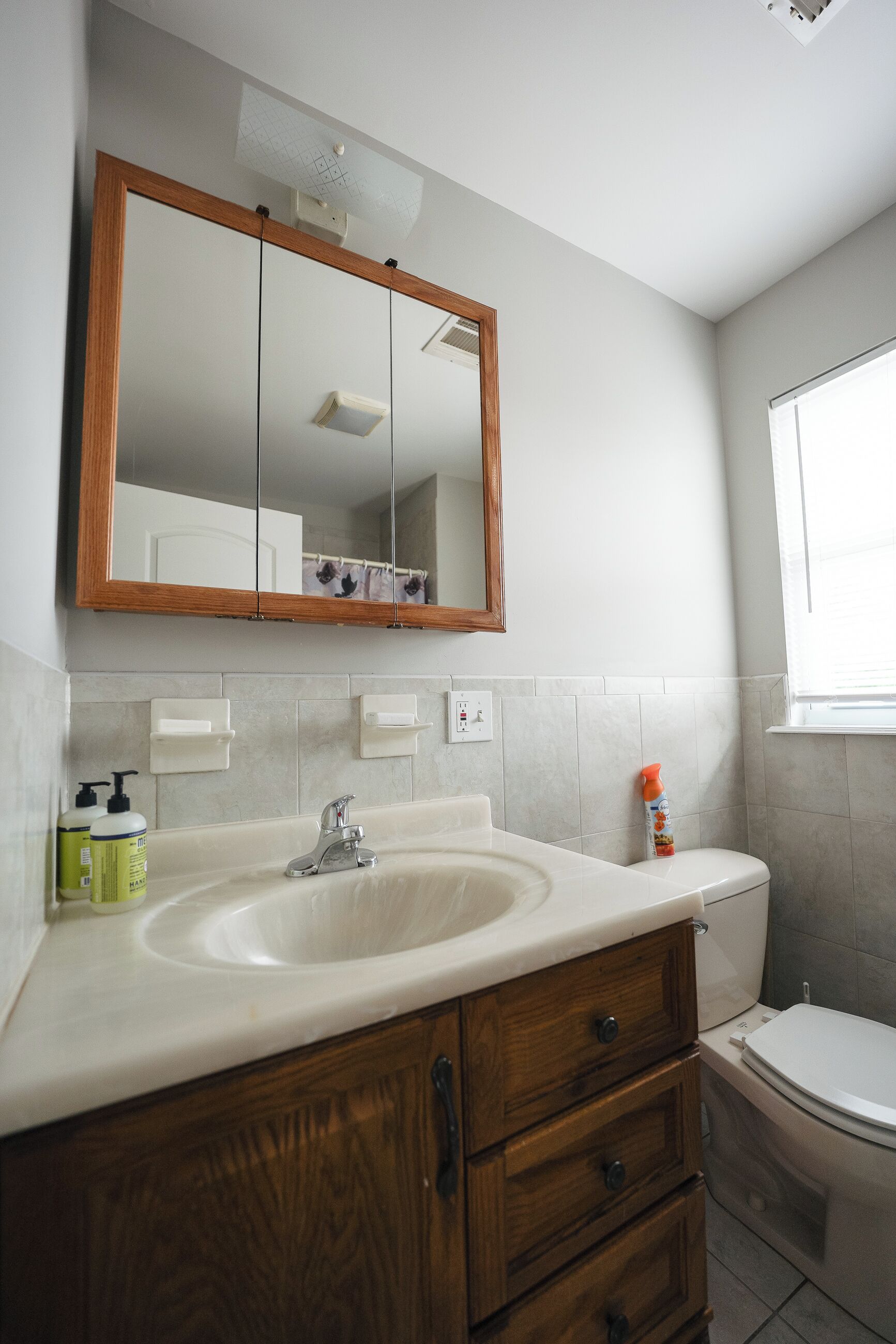 A bathroom with a wooden vanity, a sink, a mirror, and a toilet.