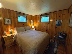 A bedroom with a bed, two bedside tables, a nightstand, a lamp, a chair, and a window.