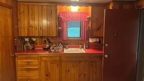 A compact kitchen with wooden cabinets, a red countertop, and a window with a view. - Charming vintage lakefront cabin w/ Wifi in BWCA (Ely)