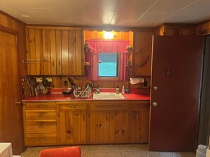 Una cocina compacta con armarios de madera, encimera roja y ventana con vistas.