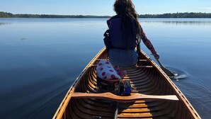 A person in a canoe on a calm lake with trees in the background. - Charming vintage lakefront cabin w/ Wifi in BWCA (Ely)