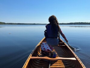 Una persona in canoa su un lago tranquillo, con alberi sullo sfondo.