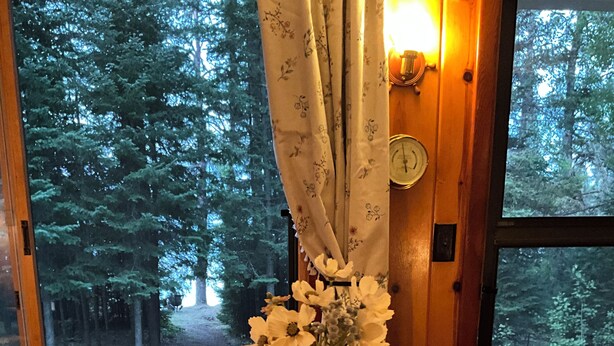 A wooden table with a white vase of flowers and a lit candle. - Charming vintage lakefront cabin w/ Wifi in BWCA (Ely)
