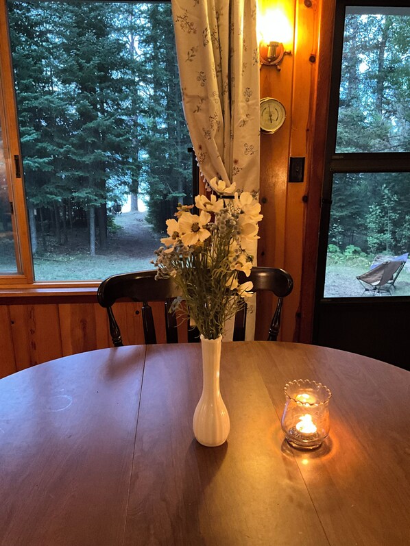 Een houten tafel met een witte vaas vol bloemen en een brandende kaars.