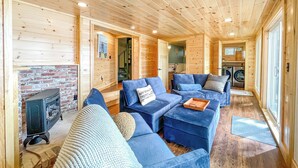 A cozy log cabin interior with a fireplace, blue upholstered furniture, and a visible laundry area.