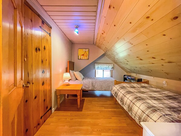 Un dormitorio acogedor en el ático con techo de madera, cama, mesita de noche, lámpara y ventana con vistas.