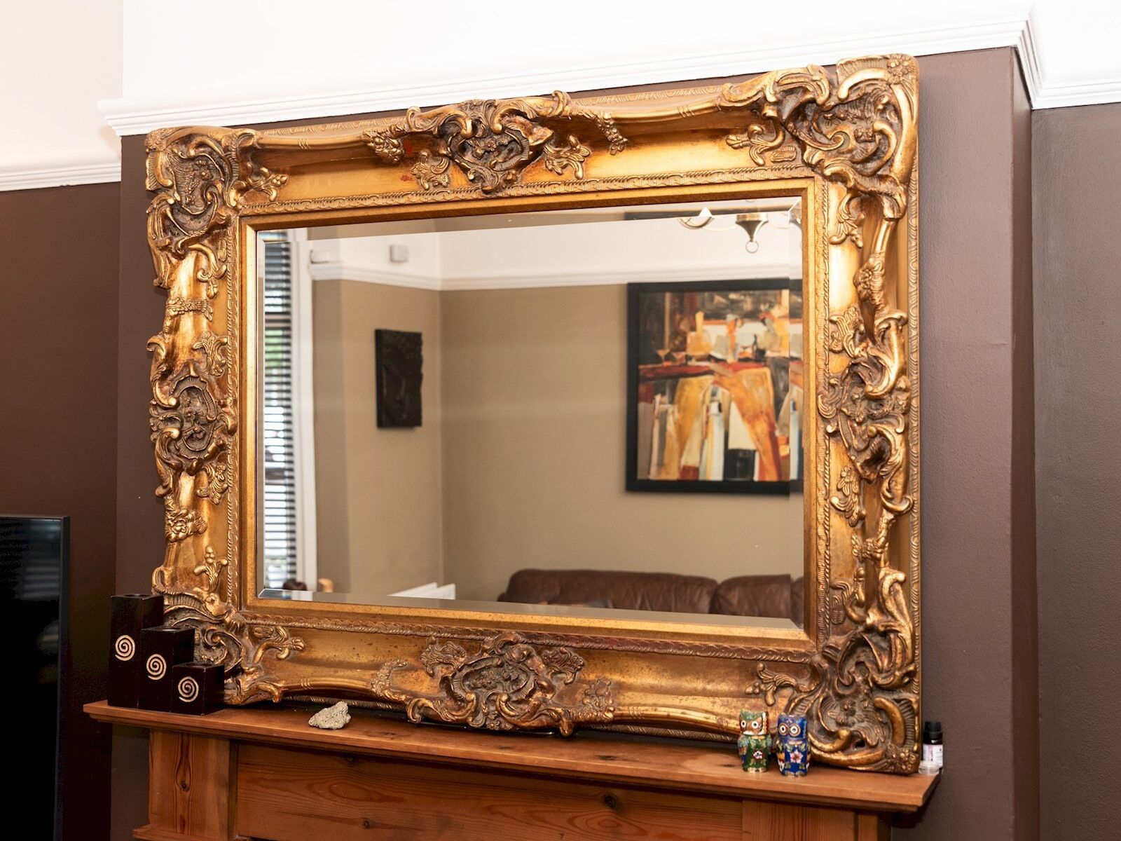 A large ornate mirror with a wooden base, set against a brown wall.
