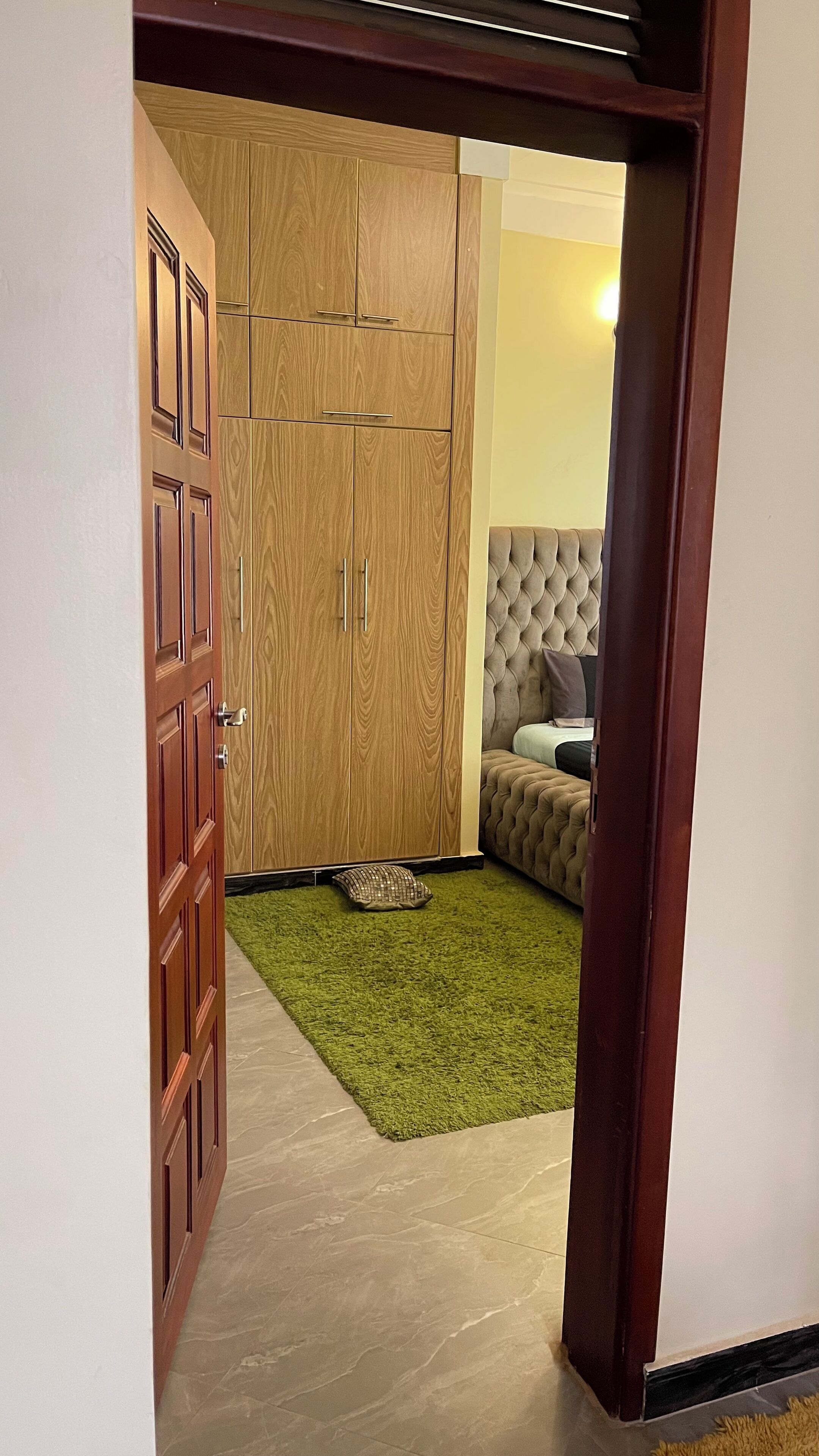 A room with a wardrobe, a bed, and a green rug.