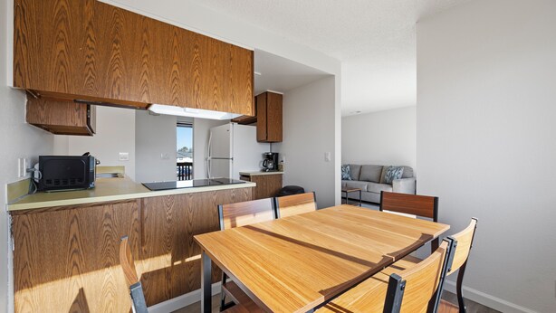 A modern kitchen with wooden cabinets, a built-in microwave, and a dining area with a wooden table and chairs.