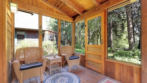 A wooden deck with wicker furniture and a round rug, overlooking a forested area.