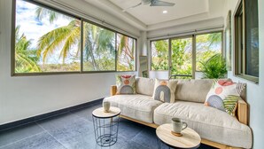 Ein modernes Wohnzimmer mit einer Couch, zwei runden Tischen und großen Fenstern mit Blick auf Palmen.