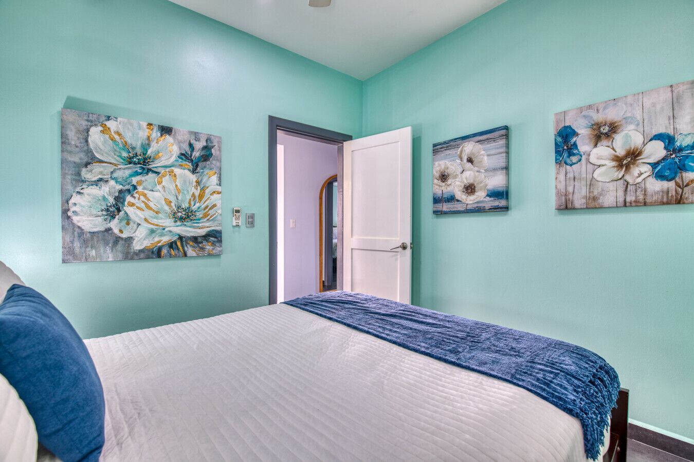 A bedroom with a bed, a door, and three floral paintings on the walls.