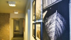 A hallway with framed pictures on the wall, a wooden door, and a stone wall on the left. - Svaleholm Gaard Roskilde -  Self check - in (Roskilde)