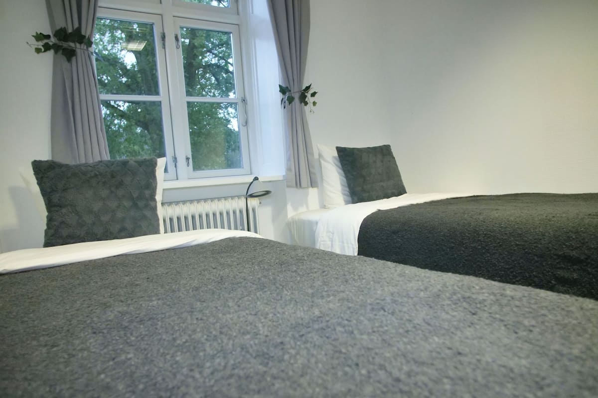 A bedroom with two beds, a window with curtains, and a radiator.