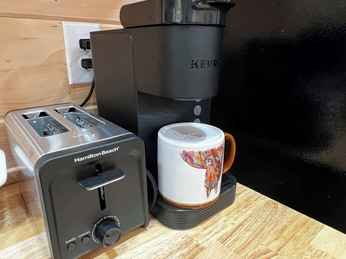 Un tostador Hamilton Beach, una cafetera Keurig y una taza sobre una superficie de madera.