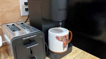 Un tostador Hamilton Beach, una cafetera Keurig y una taza sobre una superficie de madera.
