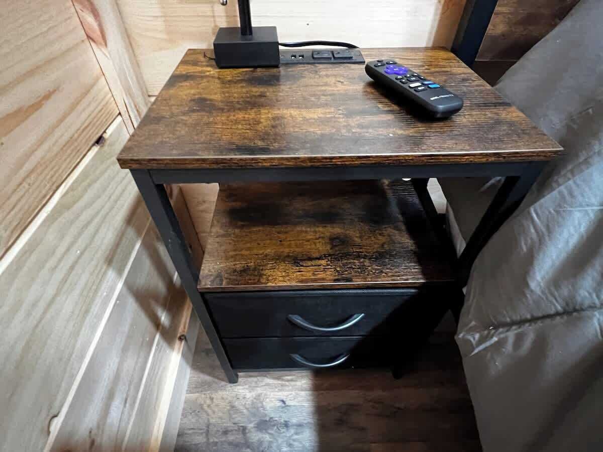 A small wooden nightstand with a remote control, a power strip, and a drawer.