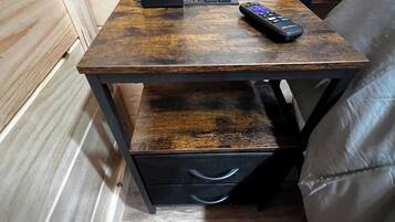 A small wooden nightstand with a remote control, a power strip, and a drawer.