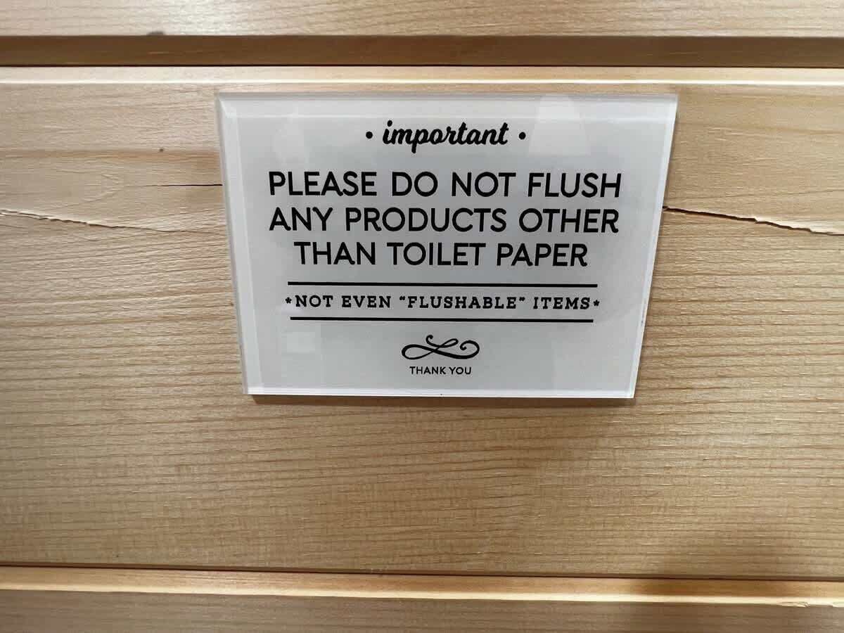 A sign on a wooden surface instructing not to flush any products other than toilet paper, even 'flushable' items.
