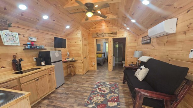 A wooden interior with a kitchen, a sofa, a ceiling fan, and a sign reading 'Backwoods Bungalow'. - Backwoods Bungalow (Pikeville)