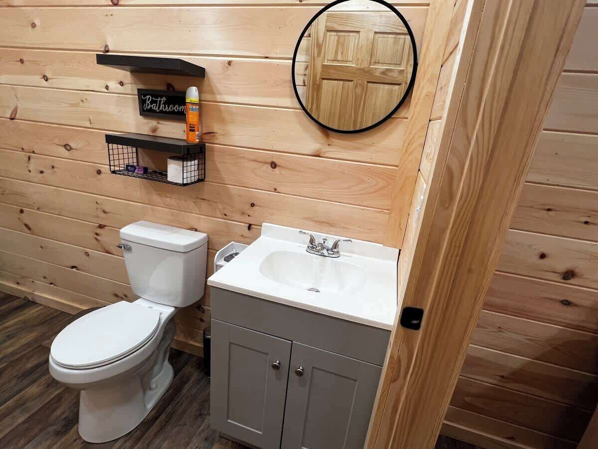A wooden-paneled bathroom with a toilet, a sink, and a small shelf with toiletries.