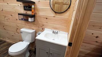 A wooden-paneled bathroom with a toilet, a sink, and a small shelf with toiletries.