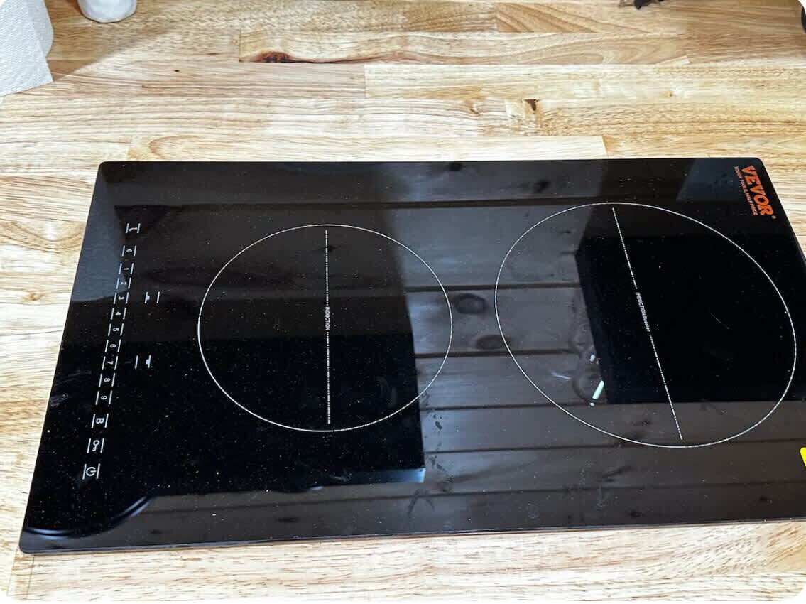 A black induction cooktop with two cooking surfaces on a wooden table.