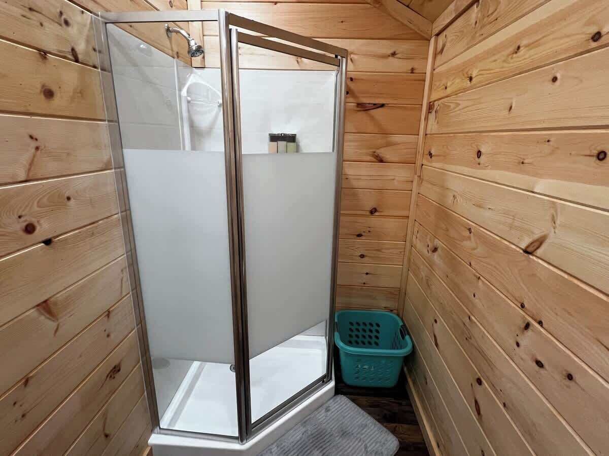 A wooden cabin with a glass-enclosed shower stall, a small blue basket, and a white sink.