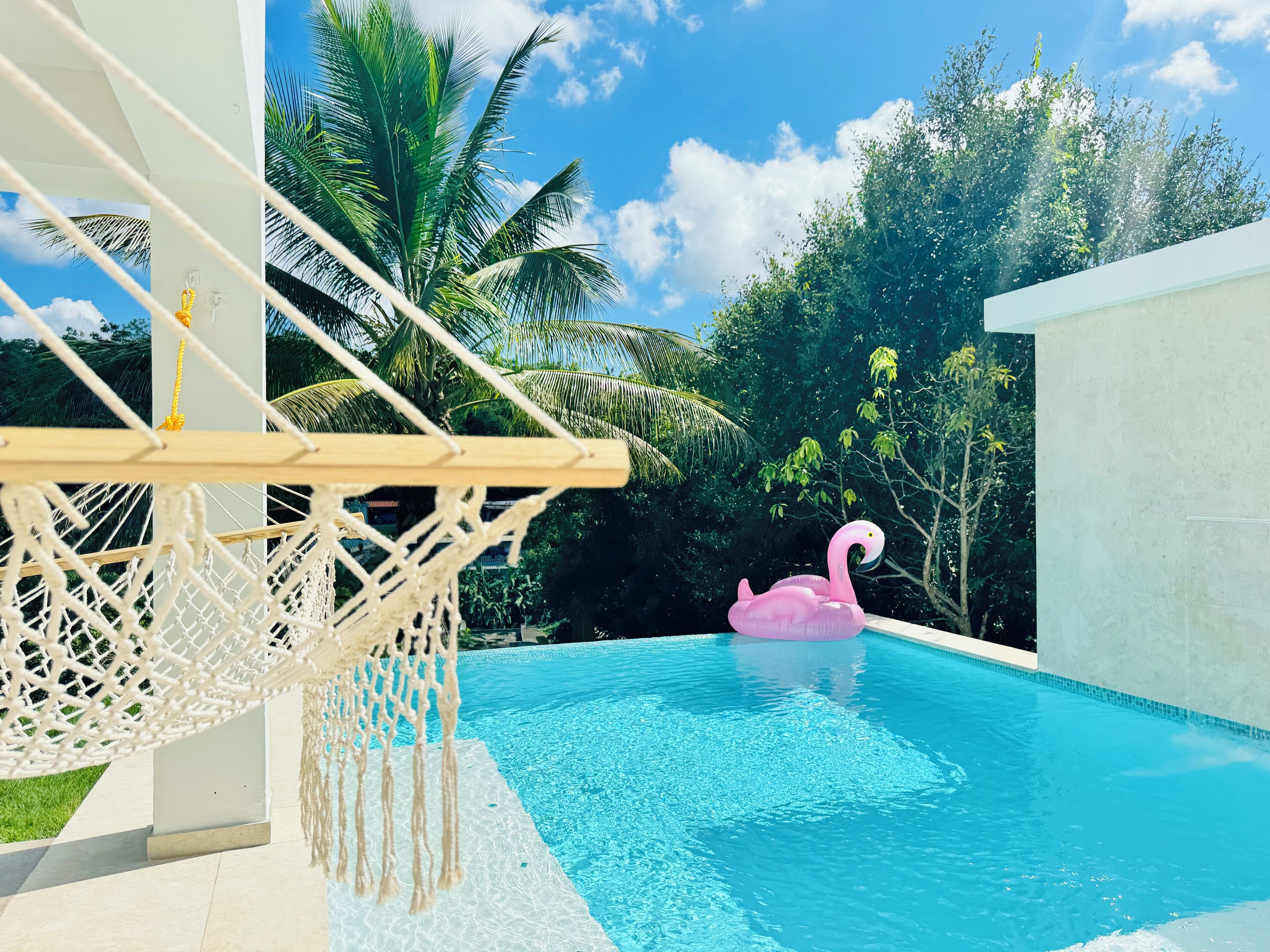 Une piscine avec un hamac en macramé et un flotteur en forme de flamant rose.