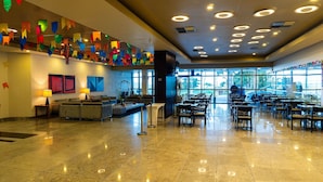 A spacious lobby with a seating area, large windows, and a ceiling with circular lights. - Flat Beach Class Internacional por Yolo  (Recife)