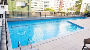 A rectangular swimming pool with clear blue water, surrounded by a tiled deck and a metal railing. - Flat Beach Class Internacional por Yolo  (Recife)