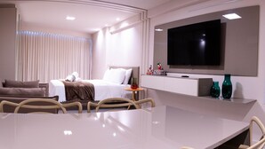 A modern hotel room with a bed, a TV, a dining table, and a seating area. - Flat Beach Class Internacional por Yolo  (Recife)