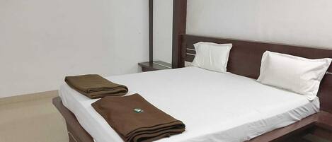 A neatly made bed with white linens and two folded brown towels on the side.