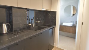 A modern kitchen with a black marble countertop, stainless steel appliances, and a built-in dishwasher. - Charming Studio with Balcony and Acropolis View (Athens)