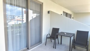 A balcony with a table and two chairs, a sliding glass door, and a view of buildings. - Charming Studio with Balcony and Acropolis View (Athens)