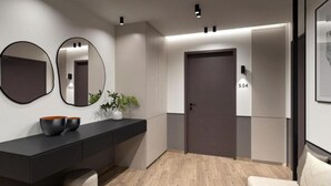 A modern hallway with a dark door marked "5.04", a black console table with decorative bowls, and two round mirrors on the wall. - Charming Studio with Balcony and Acropolis View (Athens)