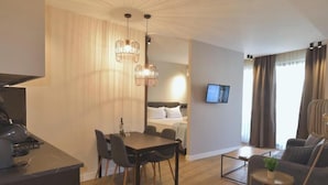 Ein modernes Wohnzimmer mit Essbereich, einer Couch, einem an der Wand befestigten Fernseher und einer Küchenzeile mit Herd.