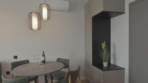 A modern dining area with a round table, six chairs, two pendant lights, and a potted plant on a black shelf. - Superior Apartment with City View (Athens)
