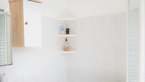 Un baño con inodoro, bañera, lavamanos, espejo y un estante con artículos de aseo.