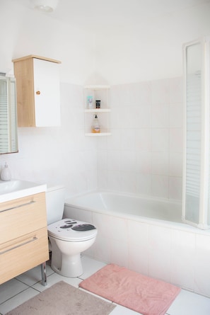A bathroom with a toilet, a bathtub, a sink, a mirror, and a shelf with toiletries.
