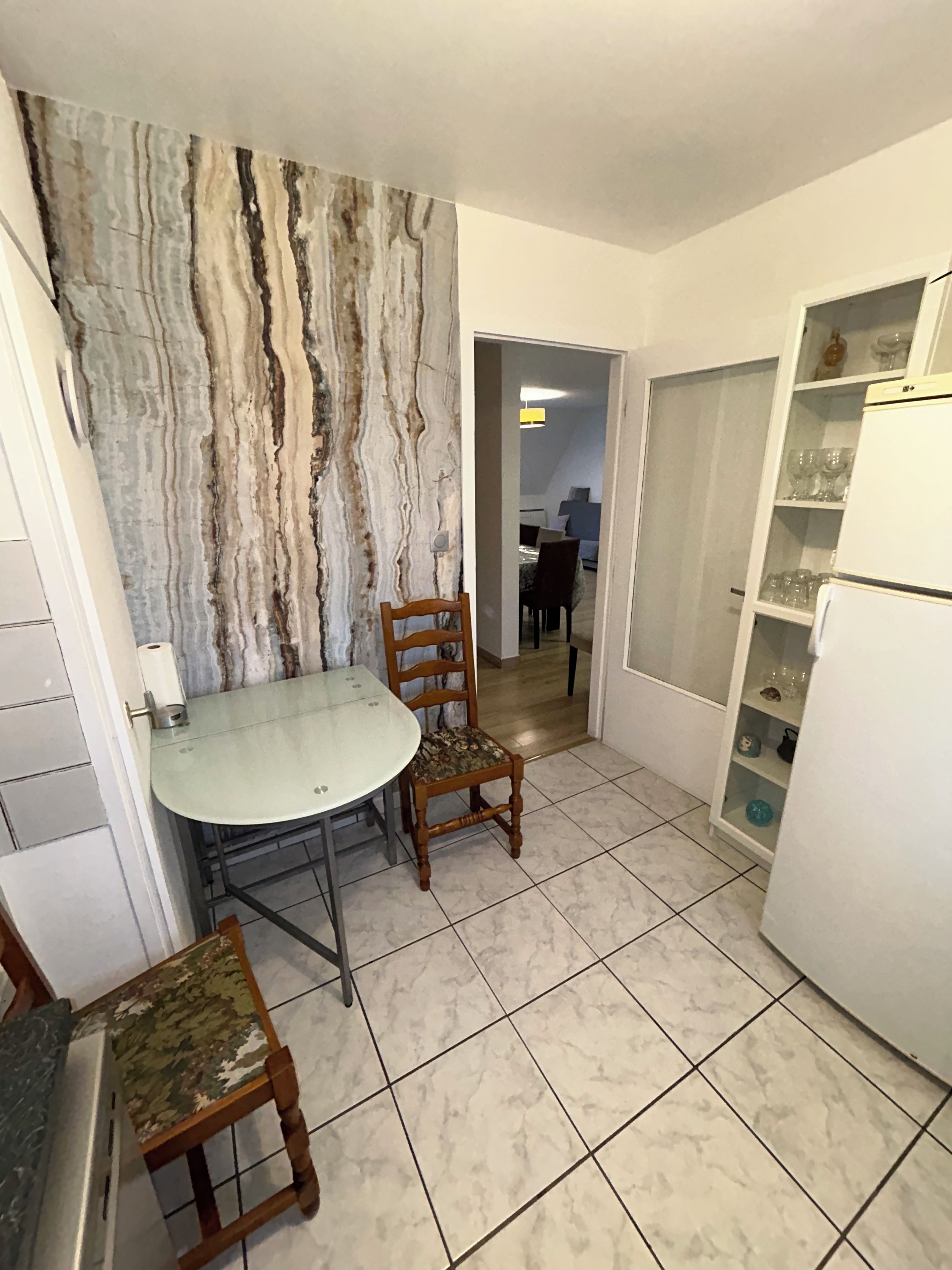 Une cuisine de taille réduite avec un pare-feu en marbre, une table à manger avec des chaises et un réfrigérateur.