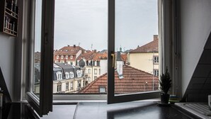 Una habitación con un ventanal grande, una planta en maceta en el alféizar y vistas a edificios cercanos.