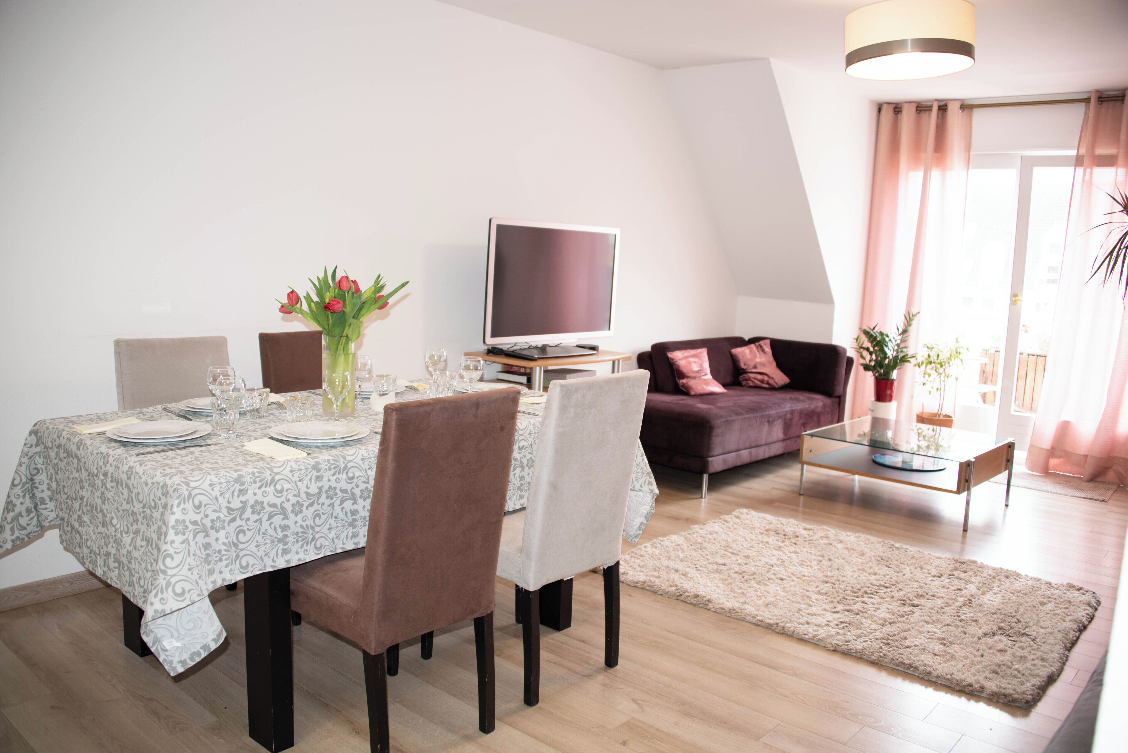 A dining area with a table set for four, a flat-screen TV, a sofa, and a coffee table.