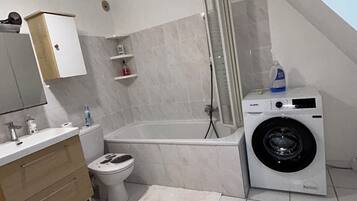 Ein modernes Badezimmer mit Toilette, Waschbecken, Waschtisch, Dusche und einer Waschmaschine.