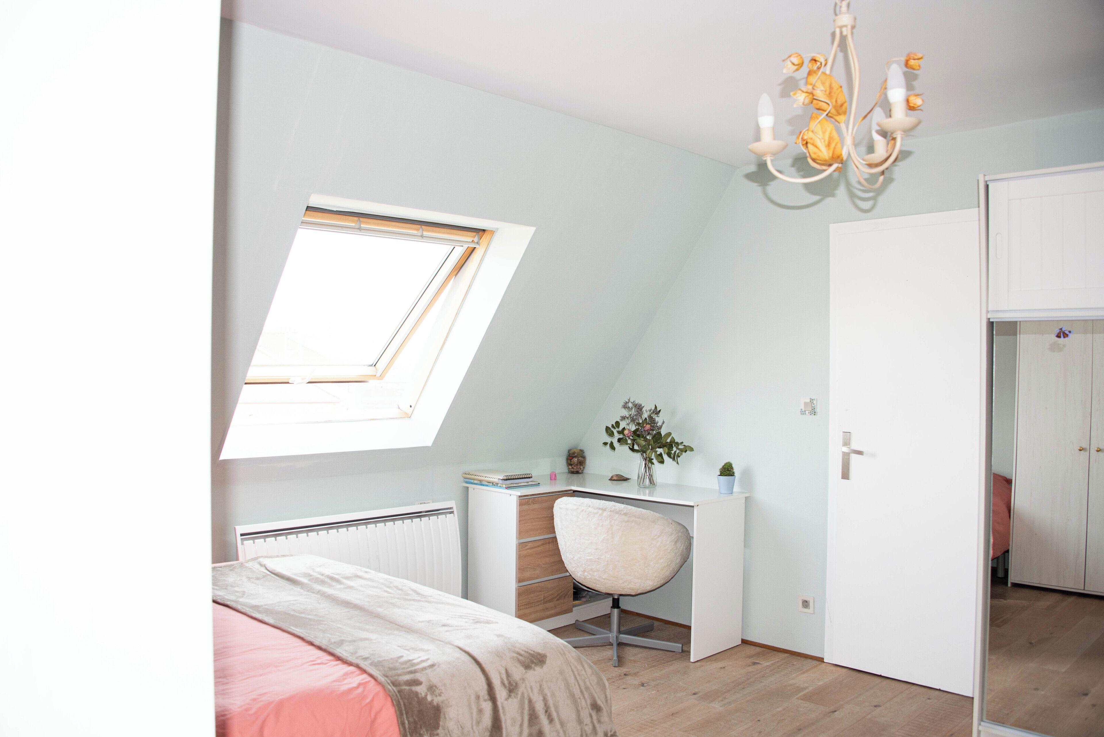 Une chambre avec un puits de lumière, un bureau, une chaise et une armoire.
