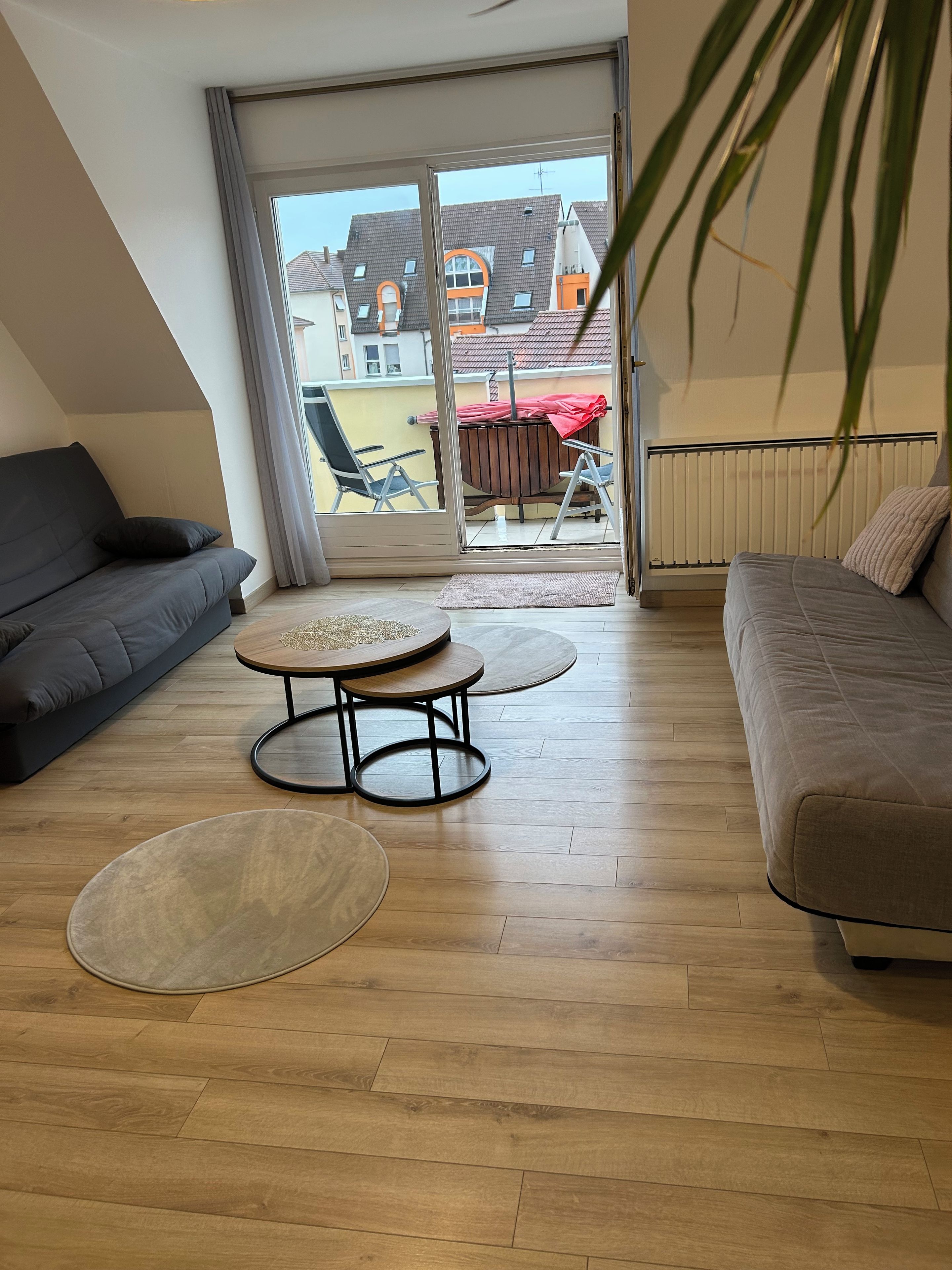 Een moderne woonkamer met een bank, een ronde salontafel en een balkon met uitzicht op gebouwen.